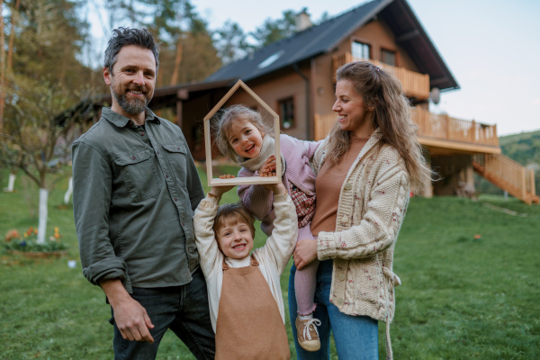 A happy family is standing near their modern house, smiling and looking at camera