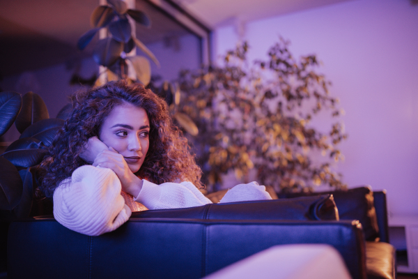 A happy young woman sitting on sofa and watching tv in living room.