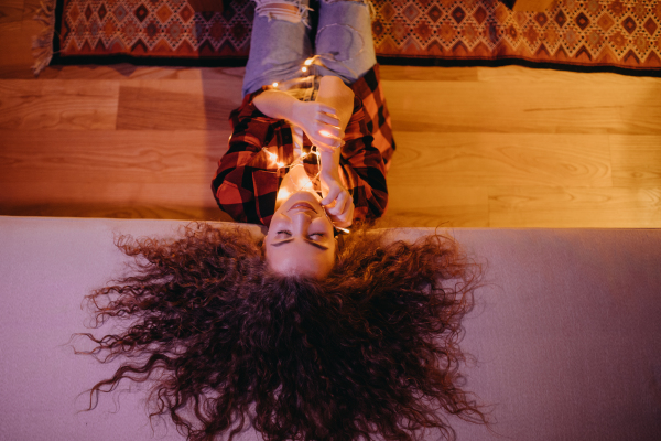 A top view of relaxed young woman with culry hair lying on sofa, hygge lifestyle.