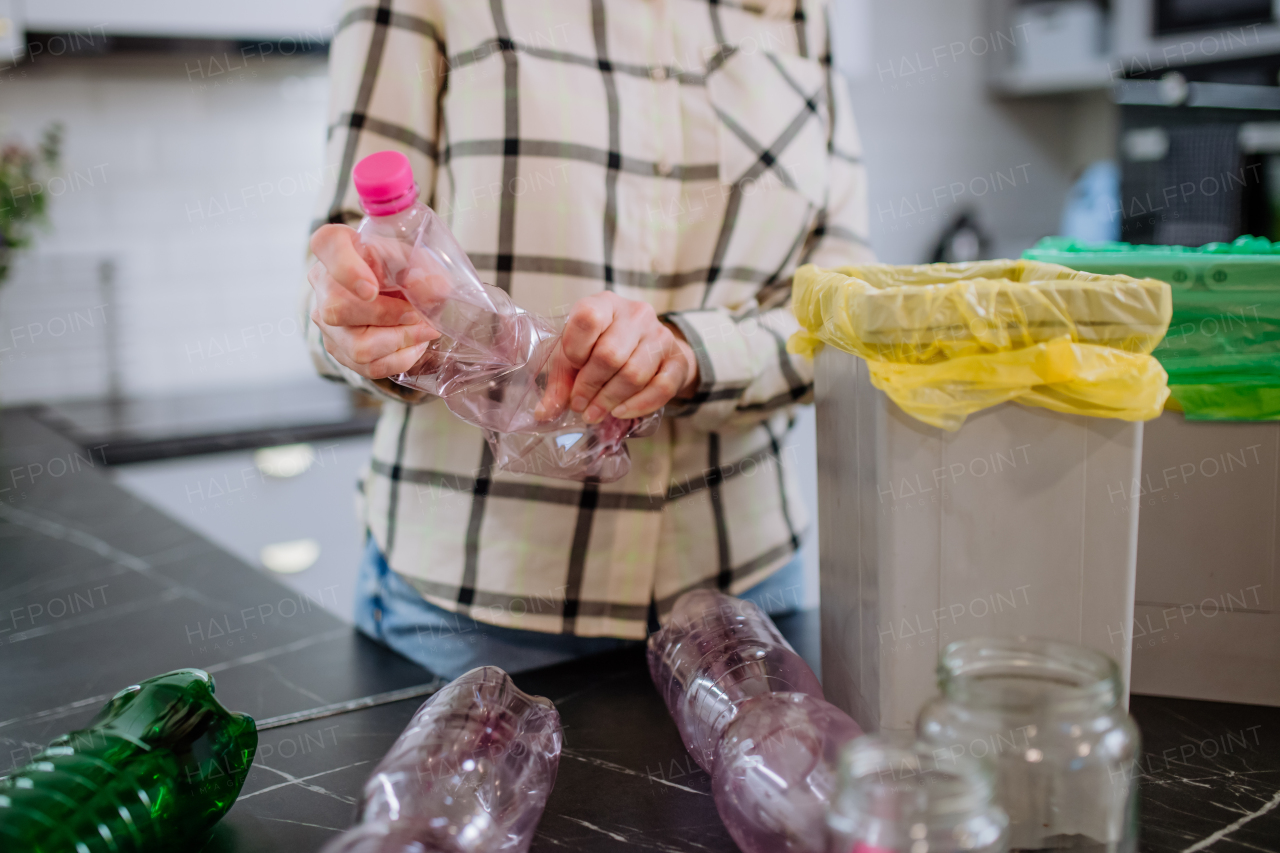 Midsection of woman throwing empty plastic bottle in recycling bin in the kitchen.