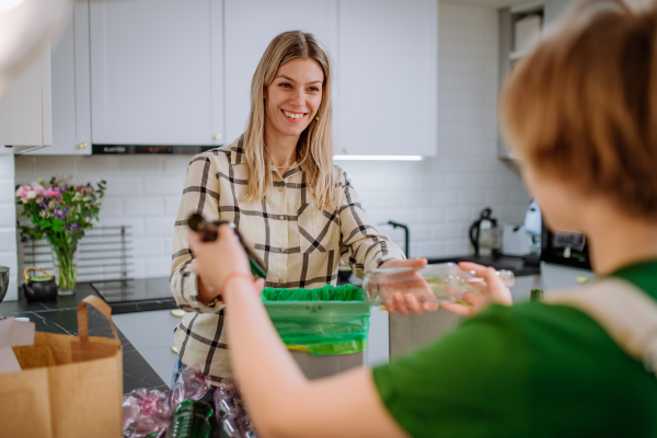 Midsection of woman throwing empty plastic bottle in recycling bin in the kitchen.