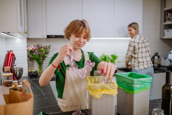 A teen girl throwing plastic bottles in recycling bin in the kitchen.