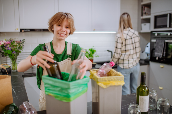 A teen girl throwing glass bottles in recycling bin in the kitchen.