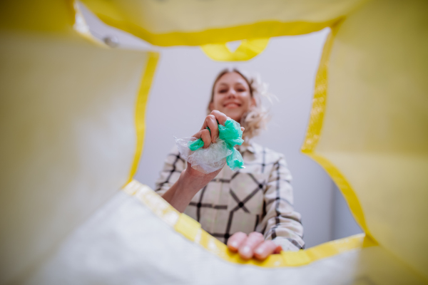 An image from inside yellow recycling bag of woman throwing a plastics to recycle.