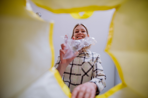 Image from inside yellow recycling bag of a woman throwing a plastic bottle to recycle.