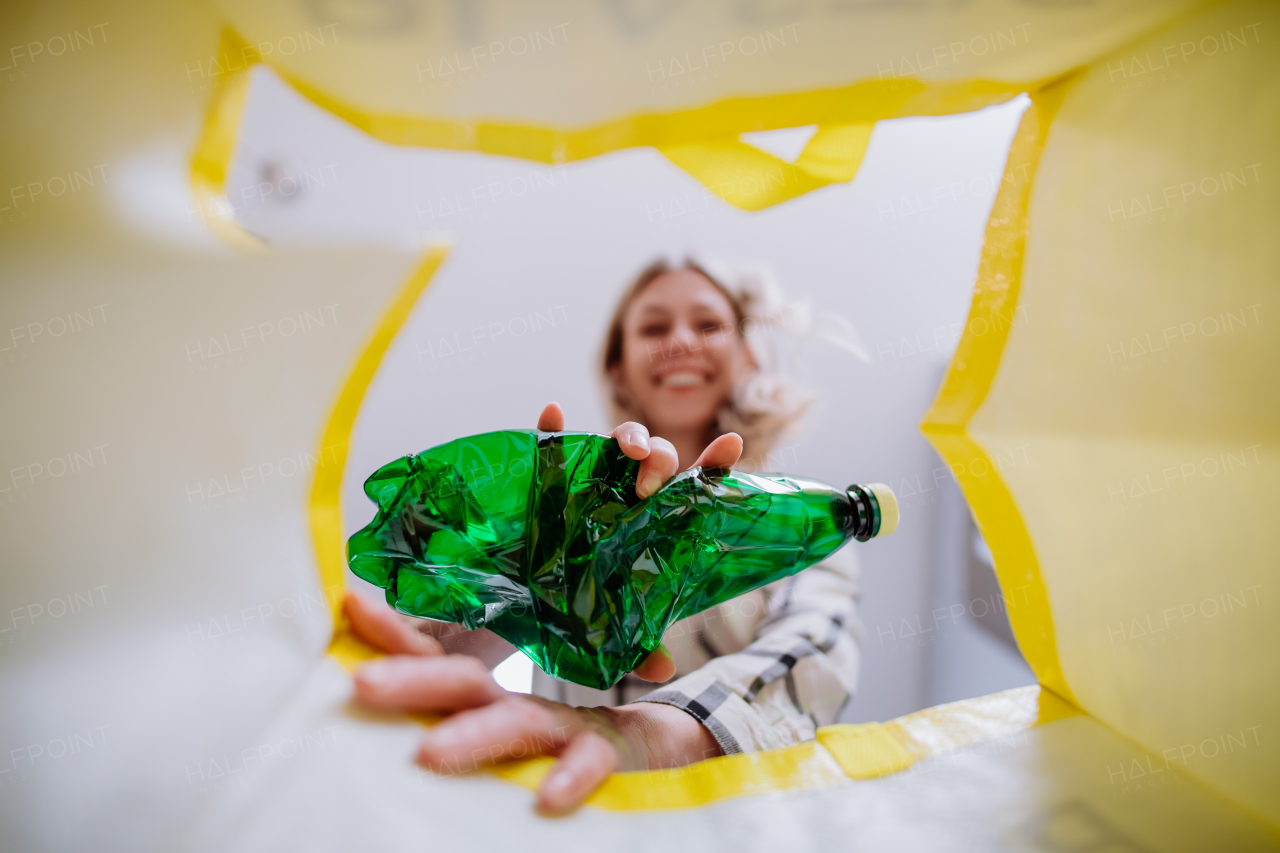 Image from inside yellow recycling bag of a woman throwing a plastic bottle to recycle.