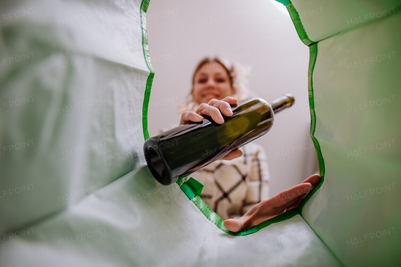 An image from inside green recycling bag of woman throwing a glass bottle to recycle.