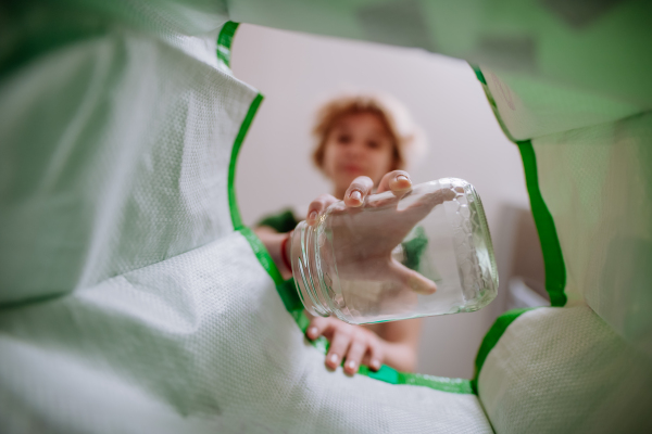 An image from inside green recycling bag of girl throwing a glass bottle to recycle.