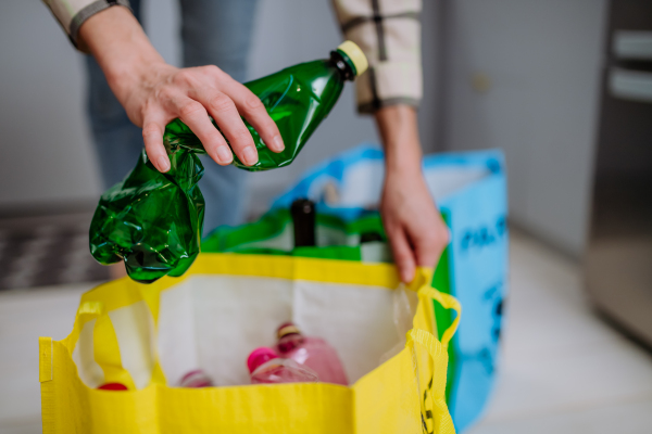 An unrecognizable woman throwing empty plastic bottle in recycling bin in kitchen.