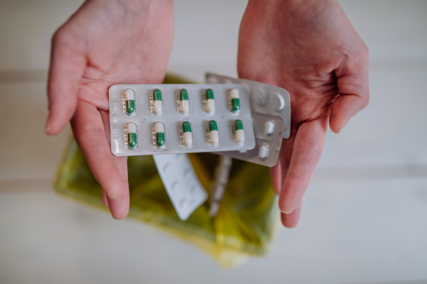 Woman's hands holding and throwing expired pills blisters to the trash bin.