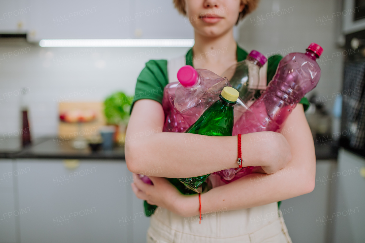 A midsection of girl holding empty plastic bottles in kitchen.