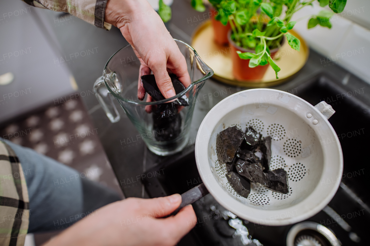 A woman cleaning shungite stones in sieve with pouring water in sink.