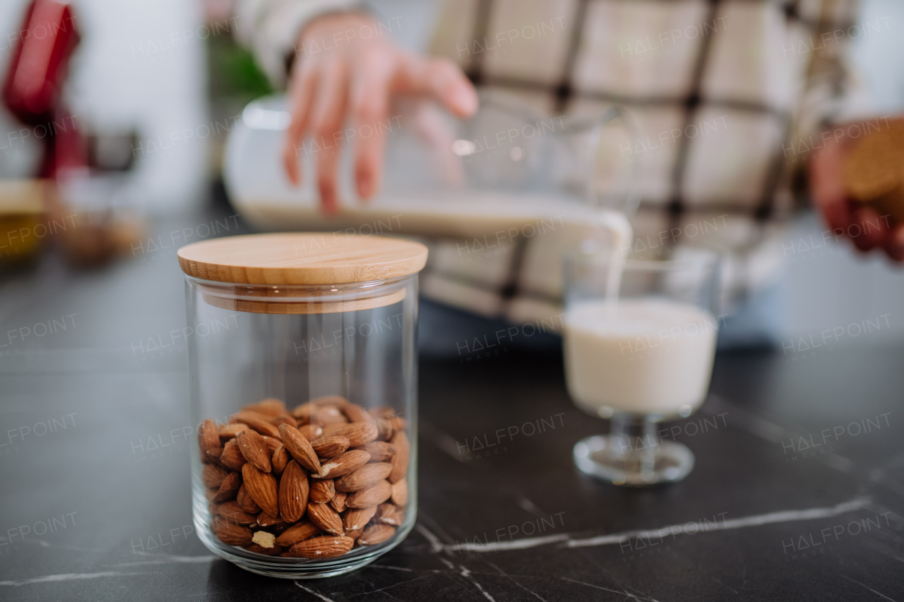 A woman pouring almond milk into a glass in kitchen. Healthy vegan product concept.