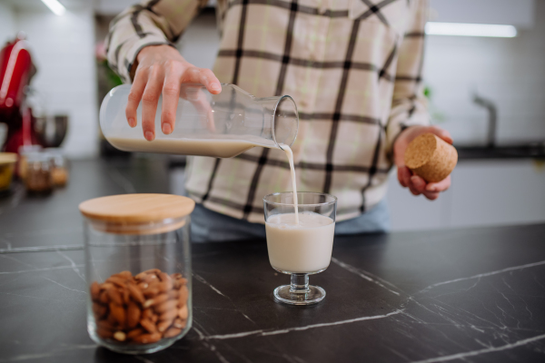 A woman pouring almond milk into a glass in kitchen. Healthy vegan product concept.