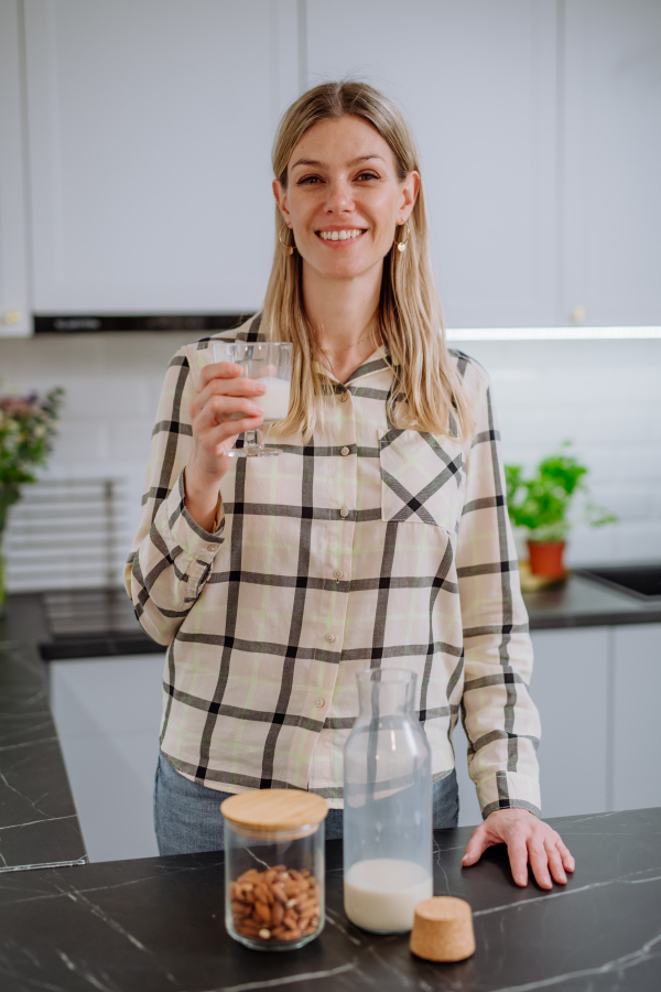 A woman holding glass with almond milk in kitchen. Healthy vegan product concept.