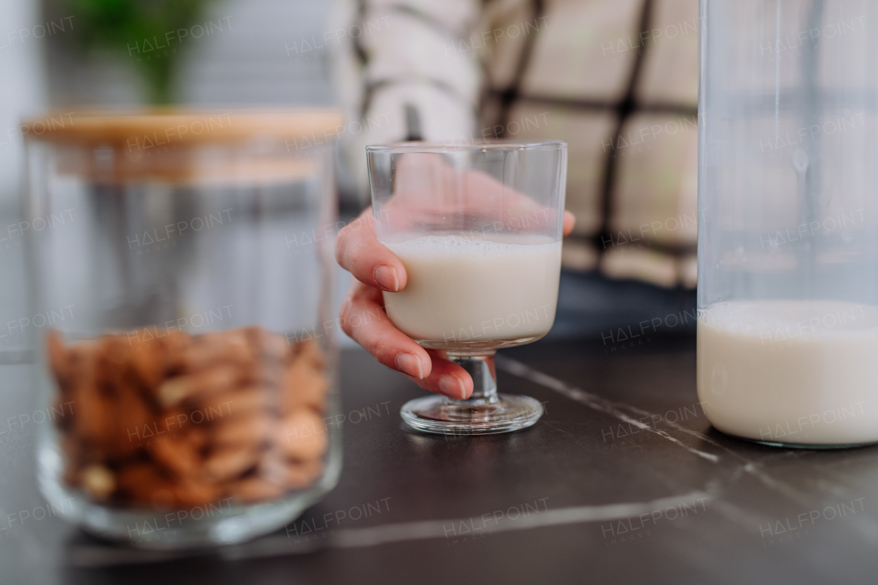 An unrecognizable woman holding glass with almond milk in kitchen. Healthy vegan product concept.