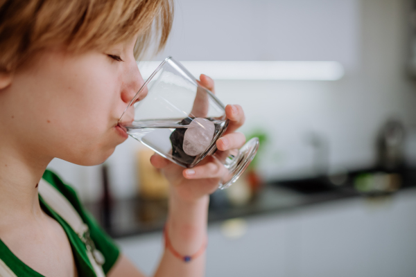 A teen girl drinking water from glass with shungite stones.