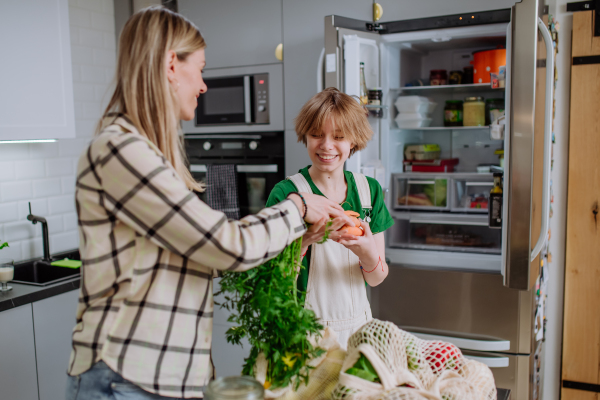 A mother unpacking local food in zero waste packaging from bag with help of daughter in kitchen at home.