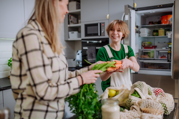 A mother unpacking local food in zero waste packaging from bag with help of daughter in kitchen at home.