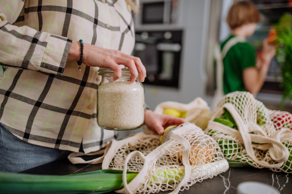 A mother unpacking local food in zero waste packaging from bag with help of daughter in kitchen at home.