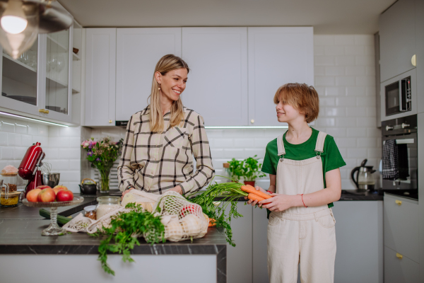 A mother unpacking local food in zero waste packaging from bag with help of daughter in kitchen at home.