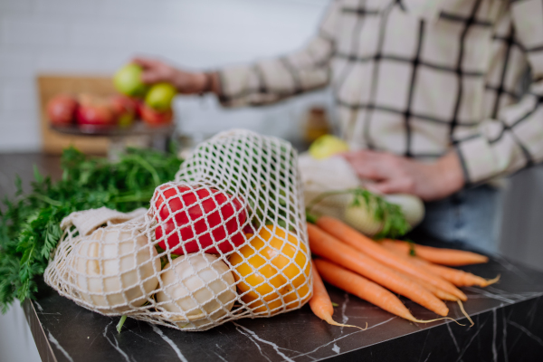 A close-up of woman unpacking shopping, vegetables and fruit in kitchen at home.