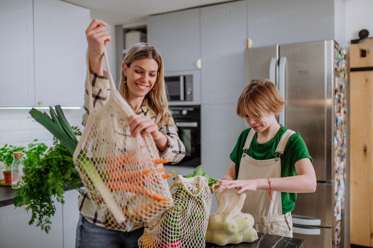 A mother unpacking local food in zero waste packaging from bag with help of daughter in kitchen at home.