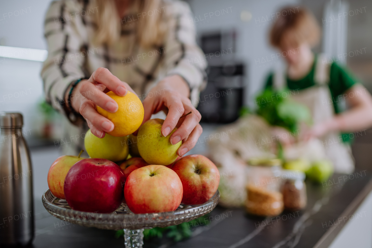 A mother unpacking shopping, vegetables and fruit, with help of daughter in kitchen at home.