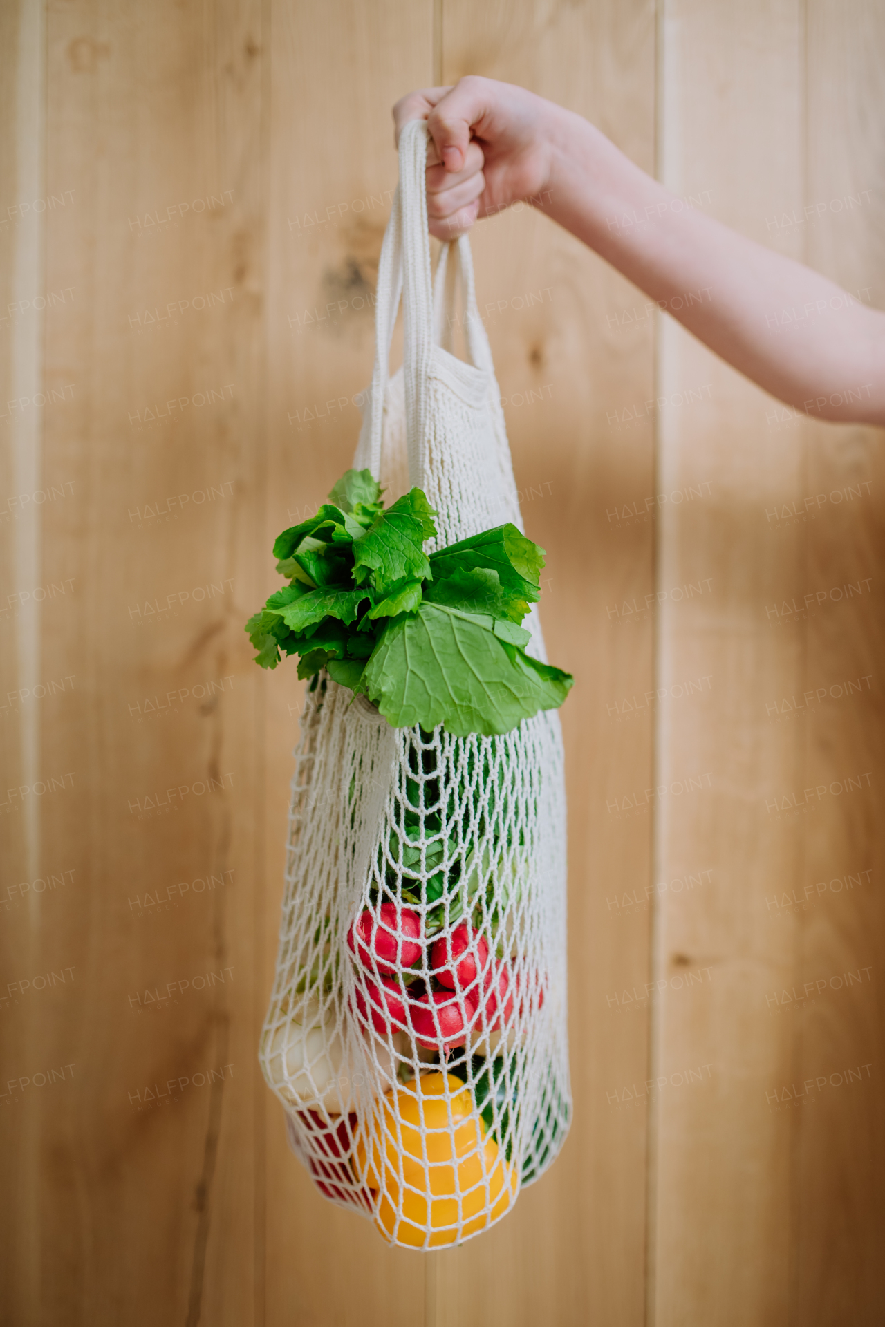 A woman holding a reusable mesh bag with fresh vegetables. Zero waste concept.