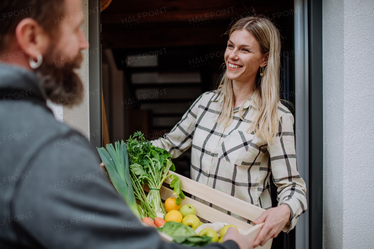 A mature man holding crate with vegetales and fruit and delivering it to woman standing at doorway.