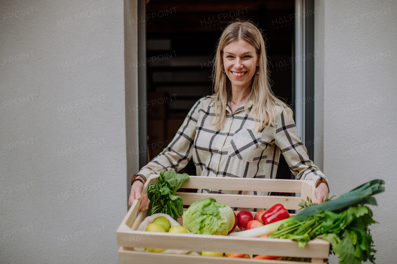 A woman holding delivered crate with vegetales and fruit from local farmer, sustainable lifestyle concept.