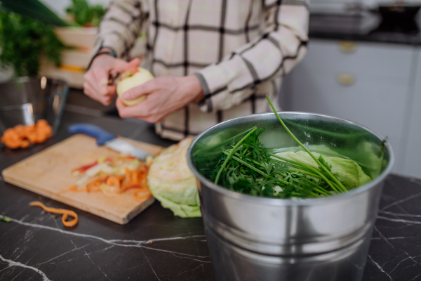 A woman throwing vegetable cuttings in a compost bucket in kitchen.