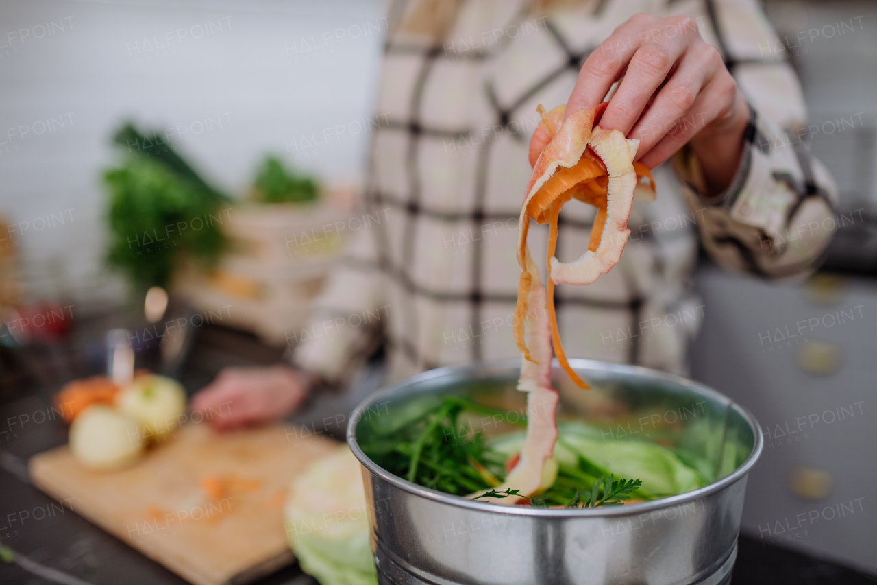 A woman throwing vegetable cuttings in a compost bucket in kitchen.