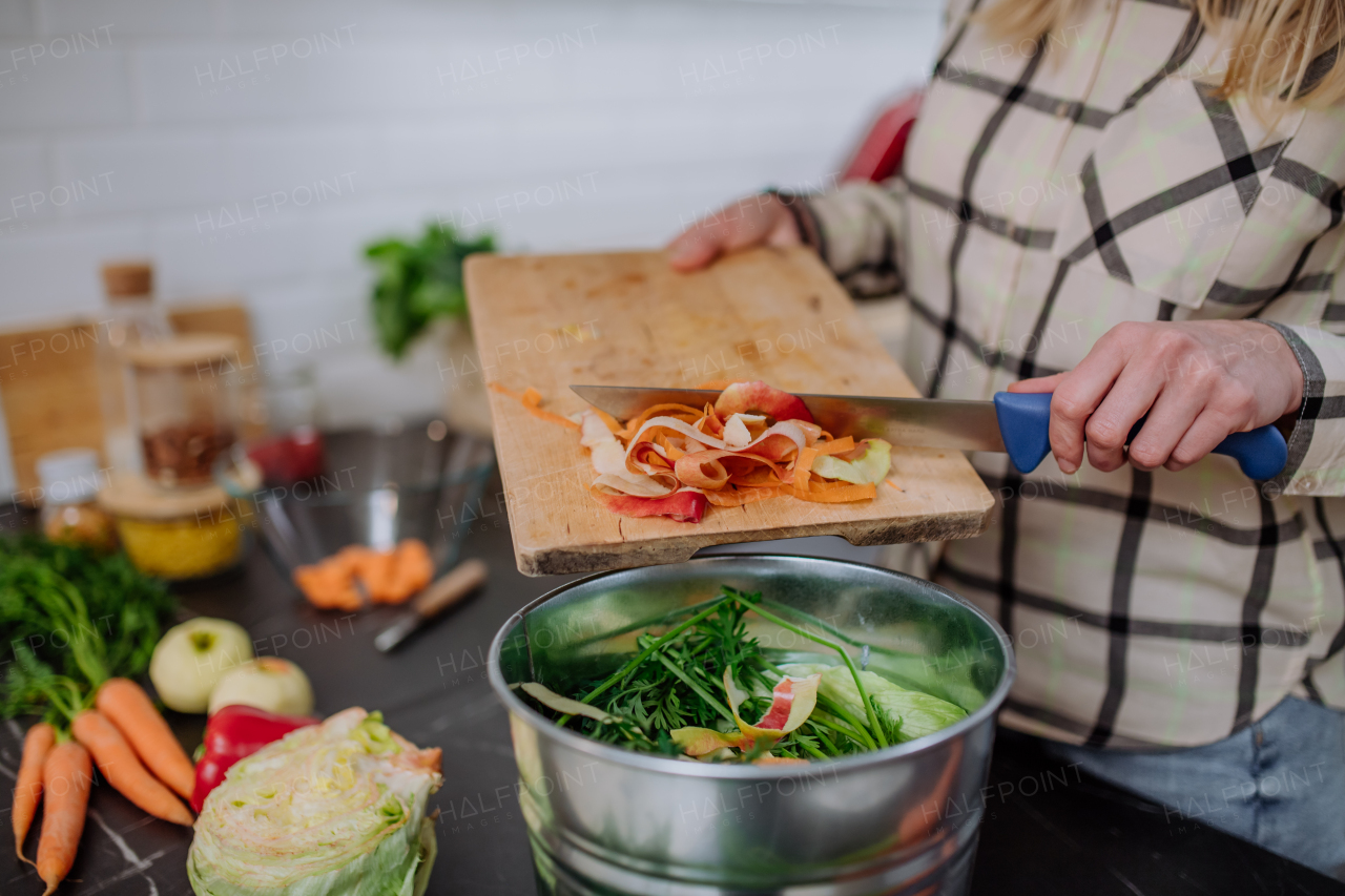 A woman throwing vegetable cuttings in a compost bucket in kitchen.