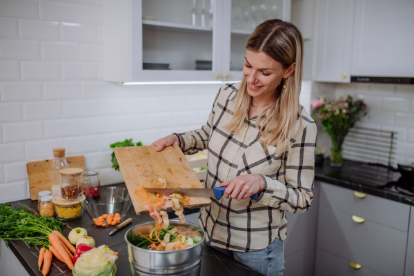 A woman throwing vegetable cuttings in a compost bucket in kitchen.