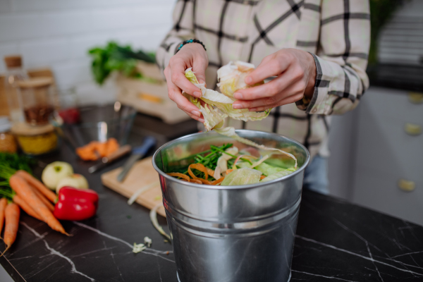 A woman throwing vegetable cuttings in a compost bucket in kitchen.