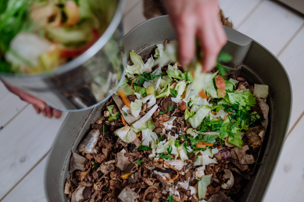 A woman throwing vegetable cuttings in a compost bucket in kitchen.