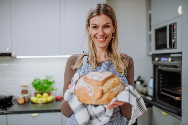 A happy woman holding homemade sourdough bread, cooking at home concept.