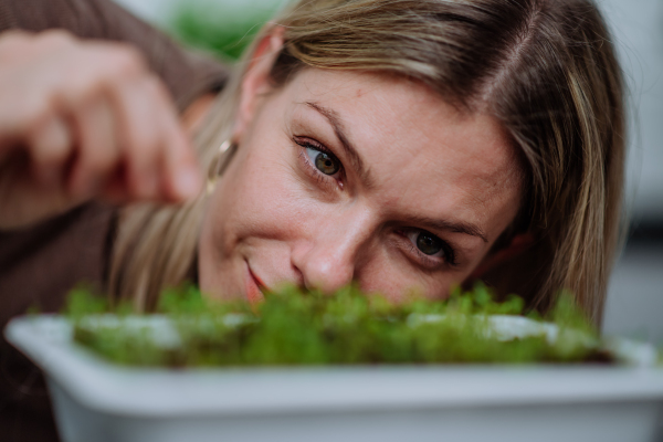 A woman looking at pot with cress growing from seed at home.