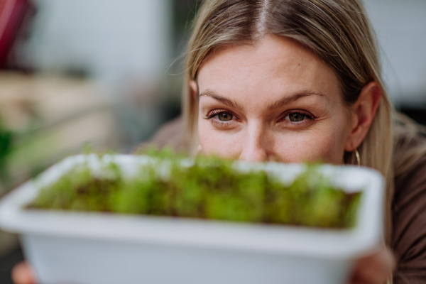 A woman holding pot with cress growing from seed at home.