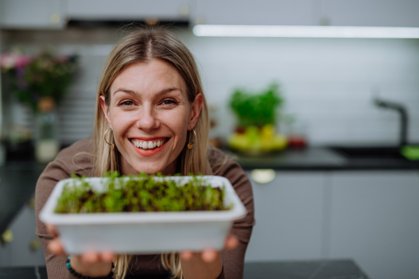 A woman holding pot with cress growing from seed at home.