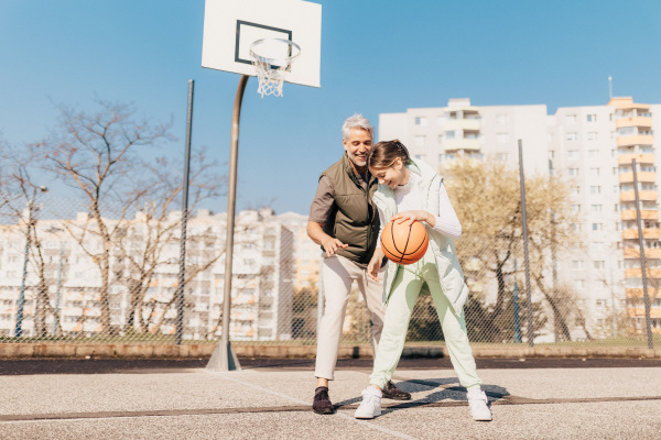 A happy father and teen daughter playing basketball outside at court.