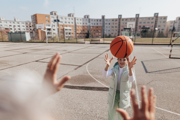 A happy father and teen daughter embracing and looking at camera outside at basketball court.