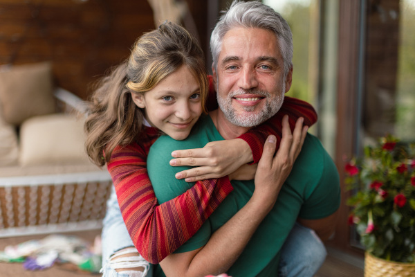 A portrait of teenage daughter hugging her happy father at home.