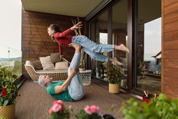 Ahappy father with teen daughter doing acrobatic exercise together at home on balcony.