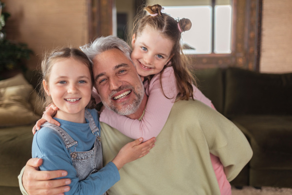 A portrait of two little daughters hugging their happy father at home.