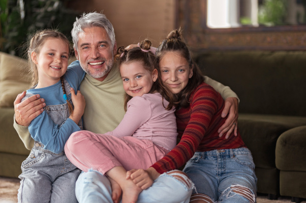 A portrait of three little daughters hugging their happy father at home.