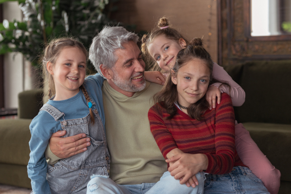 A portrait of three little daughters hugging their happy father at home.