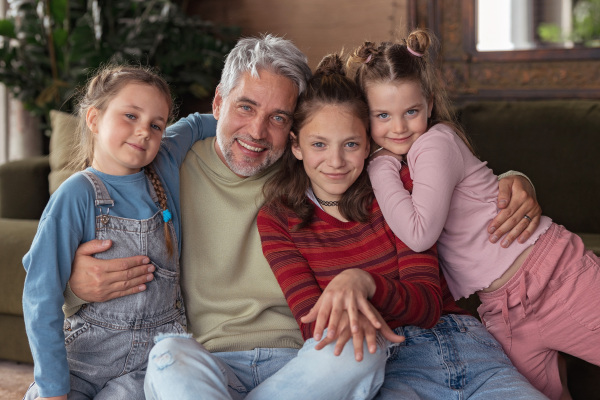 A portrait of three little daughters hugging their happy father at home.