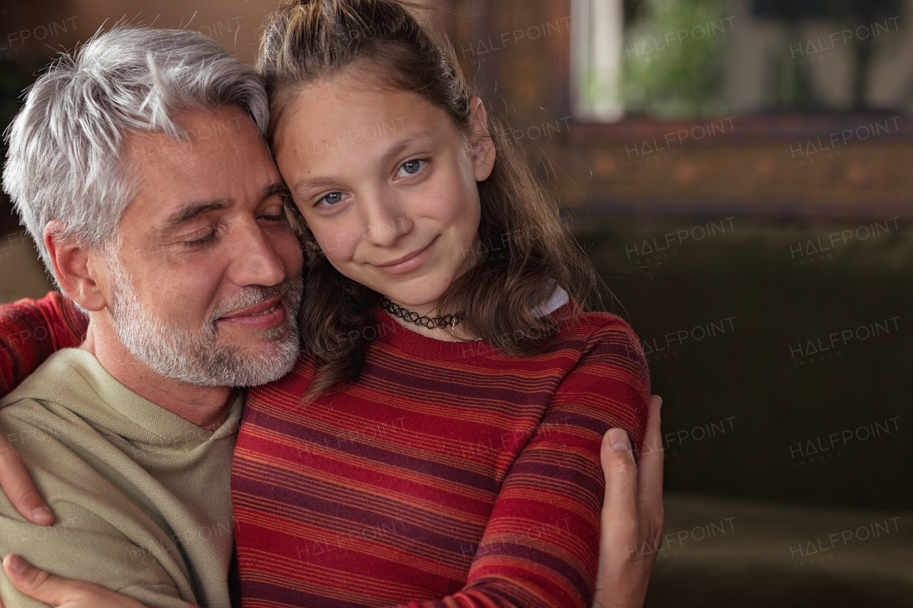 A portrait of teenage daughter hugging her happy father at home.